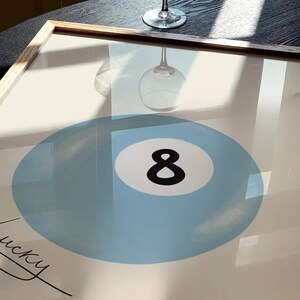 May include: A framed print of a blue billiard ball with the number 8 in black. The print is on a white background and has the word "lucky" written in black cursive.