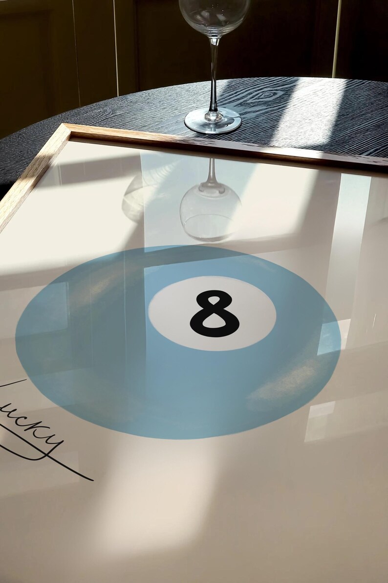 May include: A framed print of a blue billiard ball with the number 8 in black. The print is on a white background and has the word "lucky" written in black cursive.