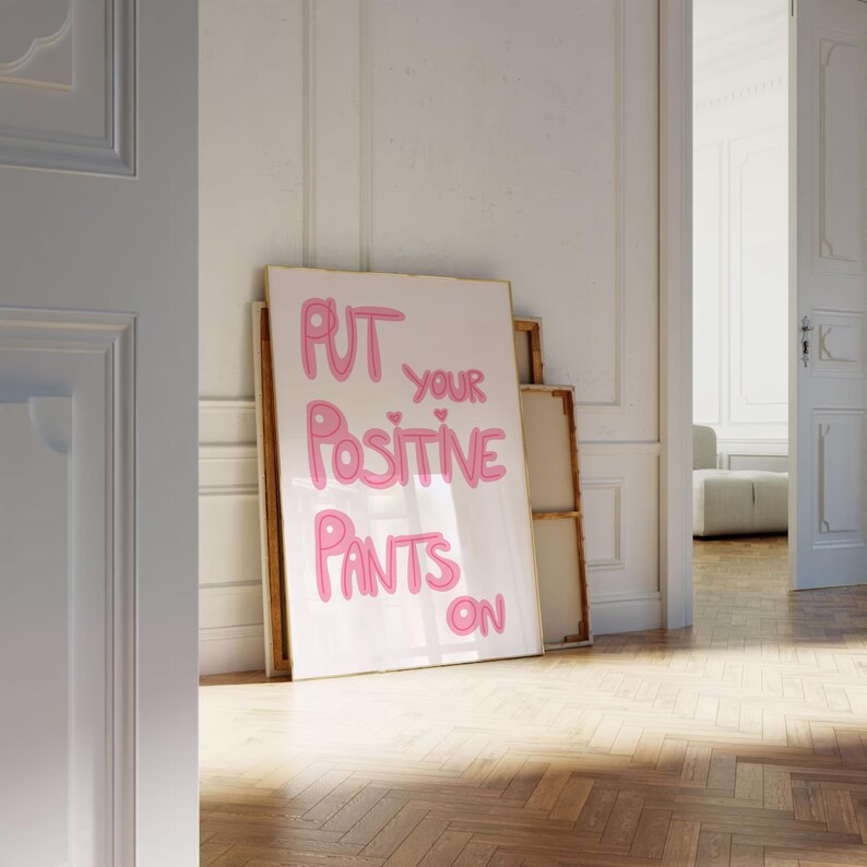 May include: A white framed poster with pink lettering that reads "Put your positive pants on".