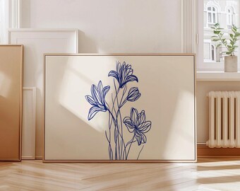 Op de afbeelding: Een ingelijste kunstdruk met een minimalistisch bloemendesign. Het kunstwerk toont blauwe lijntekeningen van bloemen op een crèmekleurige achtergrond. De lijst is van licht hout, wat een natuurlijke toets geeft. De print wordt in een lichte kamer getoond.