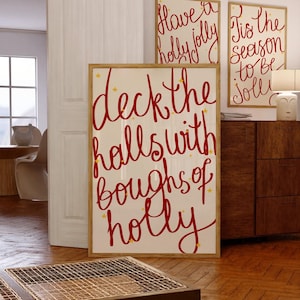 Puede incluir: Tres impresiones artísticas navideñas enmarcadas con escritura roja festiva sobre un fondo crema. La impresión más grande dice "Deck the halls with boughs of holly". Las otras dos dicen "Have a holly jolly" y "Tis the season to be jolly."