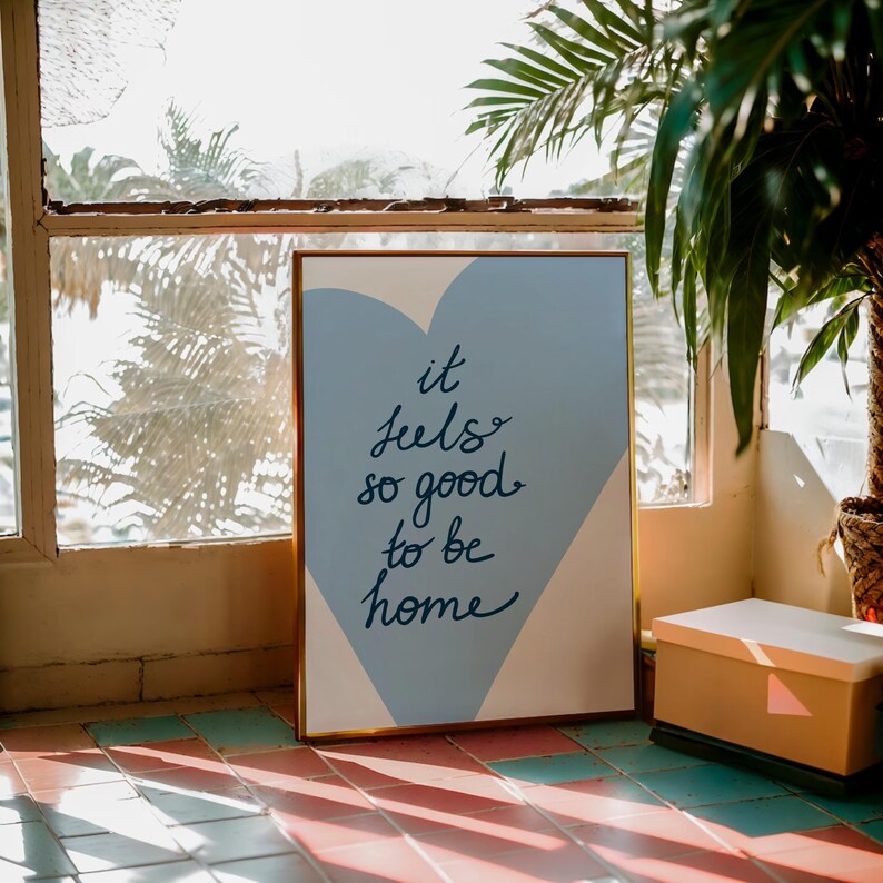 May include: A framed print with a blue and white heart design. The text on the print reads "it feels so good to be home".