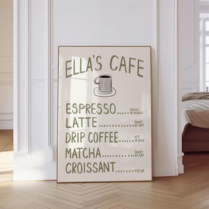 Puede incluir: Un p&oacute;ster enmarcado con el texto "ELLA'S CAFE" en verde, que enumera opciones de caf&eacute; y pasteler&iacute;a. El men&uacute; incluye espresso, latte, caf&eacute; de goteo, matcha y croissant. Un sencillo dibujo lineal de una taza de caf&eacute; est&aacute; en la parte superior.