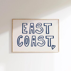 May include: A framed print with the text "EAST COAST" in a navy blue font with a heart symbol at the bottom right corner.