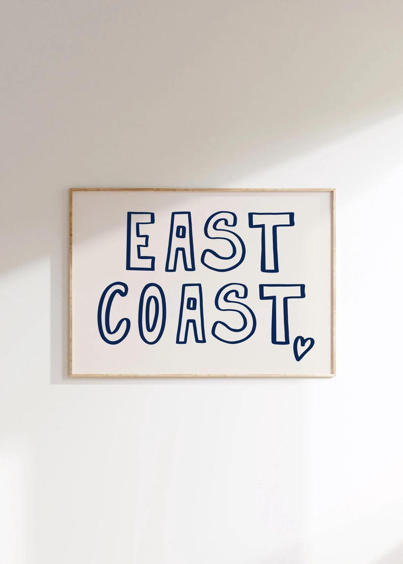 May include: A framed print with the text "EAST COAST" in a navy blue font with a heart symbol at the bottom right corner.