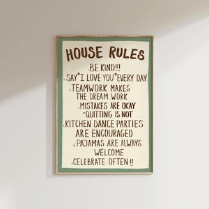 Op de afbeelding: Een rechthoekige wandkunstprint met een crèmekleurige achtergrond en een saliegroene rand. De tekst luidt: HOUSE RULES, 1. BE KIND!!!, 2. SAY "I LOVE YOU" EVERY DAY, 3. TEAMWORK MAKES THE DREAM WORK, 4. MISTAKES ARE OKAY -QUITTING IS NOT, 5. KITCHEN DANCE PARTIES ARE ENCOURAGED, 6. PAJAMAS ARE ALWAYS WELCOME, 7. CELEBRATE OFTEN !!