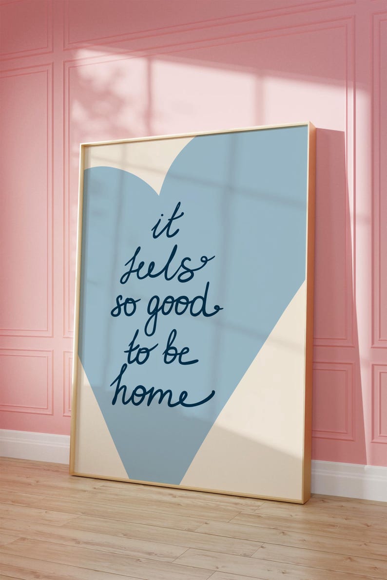 May include: A blue and cream colored poster with a heart shape in the background. The text on the poster reads "it feels so good to be home".