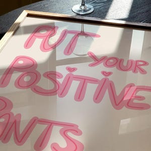 May include: A framed print with the text "Put your positive pants on" in pink lettering on a white background.