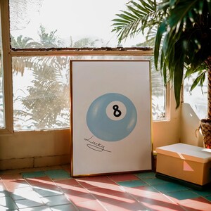 May include: A framed print of a blue billiard ball with the number 8 on it. The print has the word "Lucky" written underneath the ball.