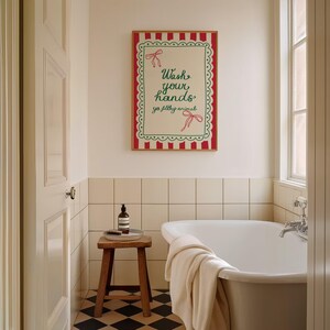 May include: A bathroom scene featuring a framed sign with the text "Wash your hands ya filthy animals." The sign has a red and white striped border and green accents. A wooden stool holds a soap bottle and brush. A white bathtub is in the background.