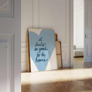 May include: A blue and white heart-shaped print with the text "it feels so good to be home" in black cursive writing.