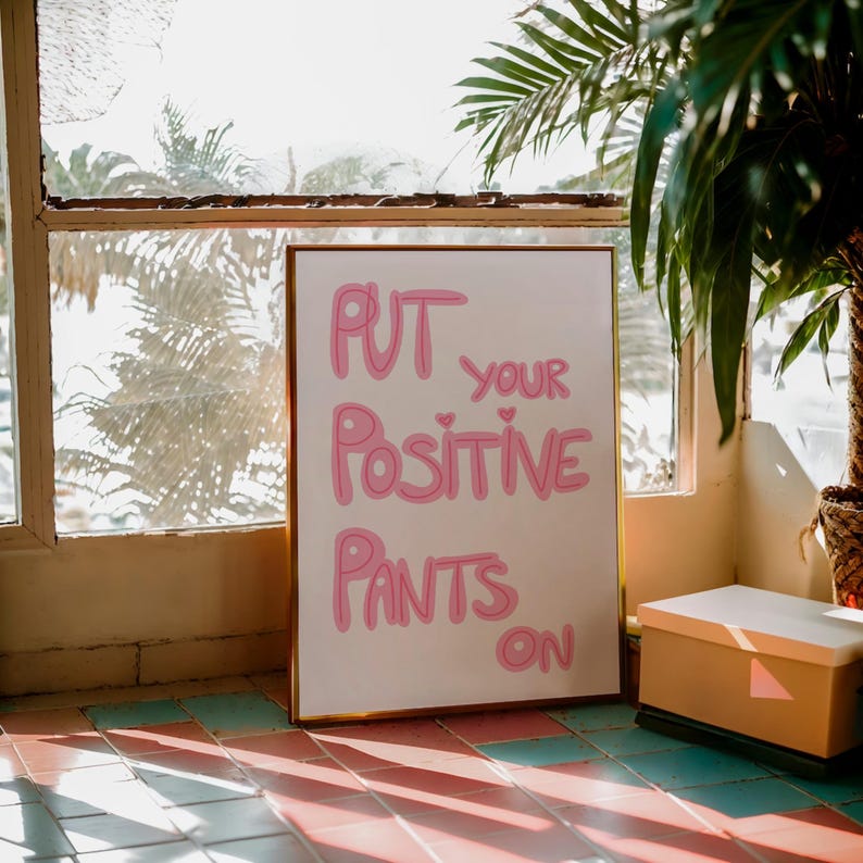 May include: A white framed poster with pink lettering that reads "Put your positive pants on".