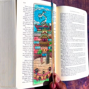 May include: A colorful bookmark featuring a detailed illustration of a pagoda-style building with a dragon and text from "The Lord of the Rings." The bookmark is inserted into an open book.