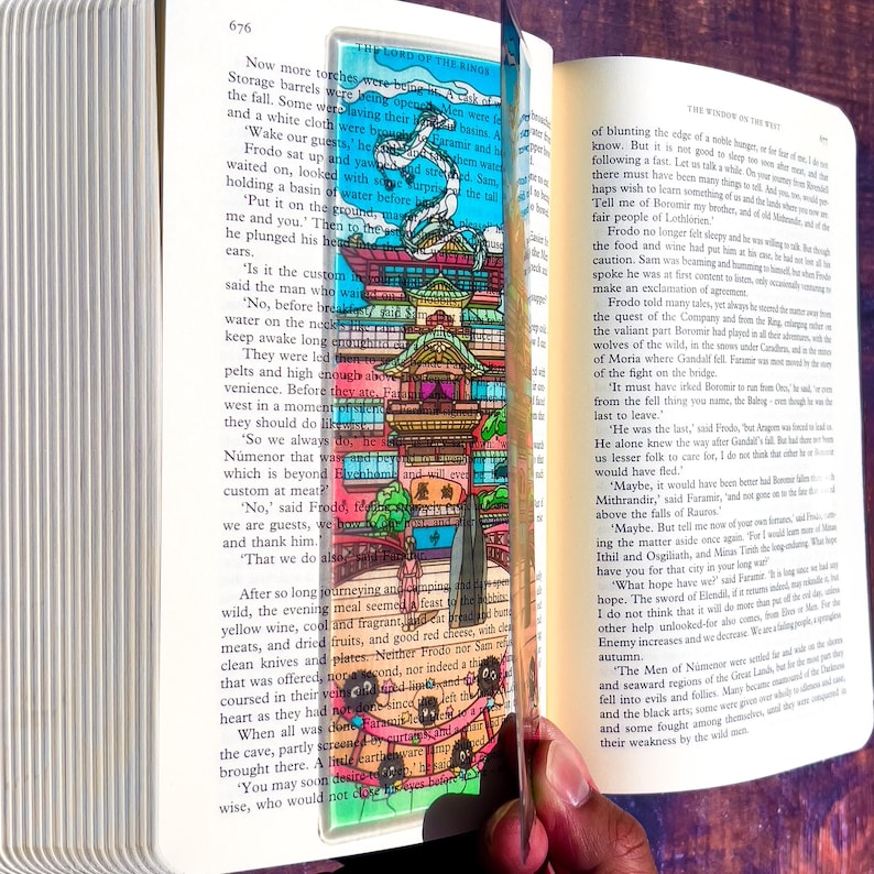 May include: A colorful bookmark featuring a detailed illustration of a pagoda-style building with a dragon and text from "The Lord of the Rings." The bookmark is inserted into an open book.