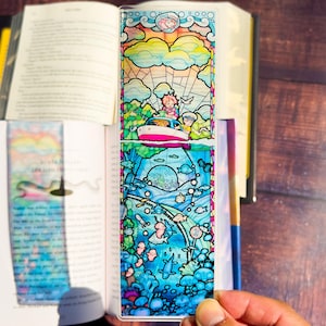 May include: A colorful, stained-glass style bookmark featuring a boat on the water and an underwater scene. The top portion shows a boat with two people, clouds, and a sun. The bottom half depicts an underwater scene with fish and coral.