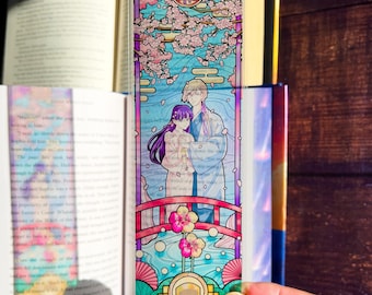 May include: A clear, rectangular bookmark featuring a stained-glass style illustration of two figures on a bridge, with cherry blossoms and a river. The bookmark has a purple, blue, and pink color scheme.