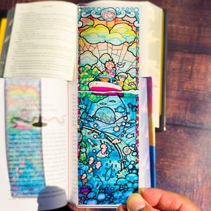 May include: A colorful, stained-glass style bookmark featuring a boat on the water and an underwater scene. The top portion shows a boat with two people, clouds, and a sun. The bottom half depicts an underwater scene with fish and coral.