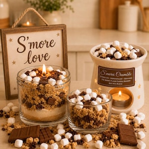 May include: A collection of S'mores-themed soy wax candles and a warmer. One candle in a glass jar is lit, topped with marshmallow and chocolate pieces. A smaller glass jar and a ceramic warmer labeled S'mores Crumble also feature these toppings.