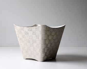 May include: A white ceramic planter with a geometric pattern. The planter has a wide, square base and a flared top.