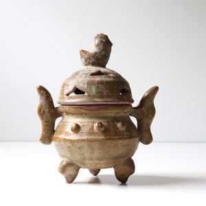 May include: A ceramic incense burner with a bird-shaped lid and three legs. The burner is decorated with a brown and white glaze.