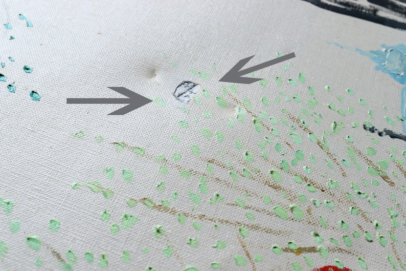 May include: A close-up of a white canvas with a hole in the center. The canvas is covered in small green and gold paint splatters. Two arrows point to the hole.