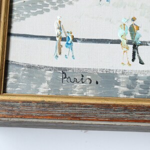 May include: A framed painting of a city scene with people walking on a street. The painting is signed "Paris." in the bottom right corner.