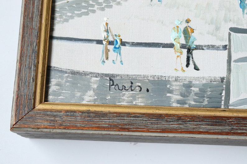 May include: A framed painting of a city scene with people walking on a street. The painting is signed "Paris." in the bottom right corner.