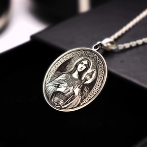 A silver pendant featuring an engraved image of a woman with a halo, possibly representing a religious figure.
