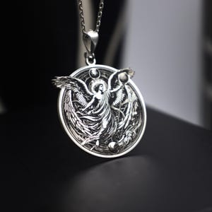 May include: Silver pendant necklace featuring an intricate design of an angel with outstretched wings, holding a sphere in one hand. The angel is surrounded by a circular frame with celestial symbols.
