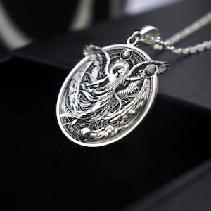 May include: A silver pendant necklace featuring an intricate design of an angel with outstretched wings. The angel is surrounded by a circular frame with celestial details.