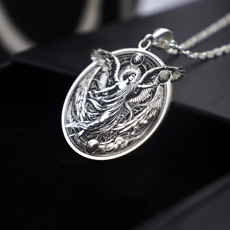 May include: A silver pendant necklace featuring an intricate design of an angel with outstretched wings. The angel is surrounded by a circular frame with celestial details.