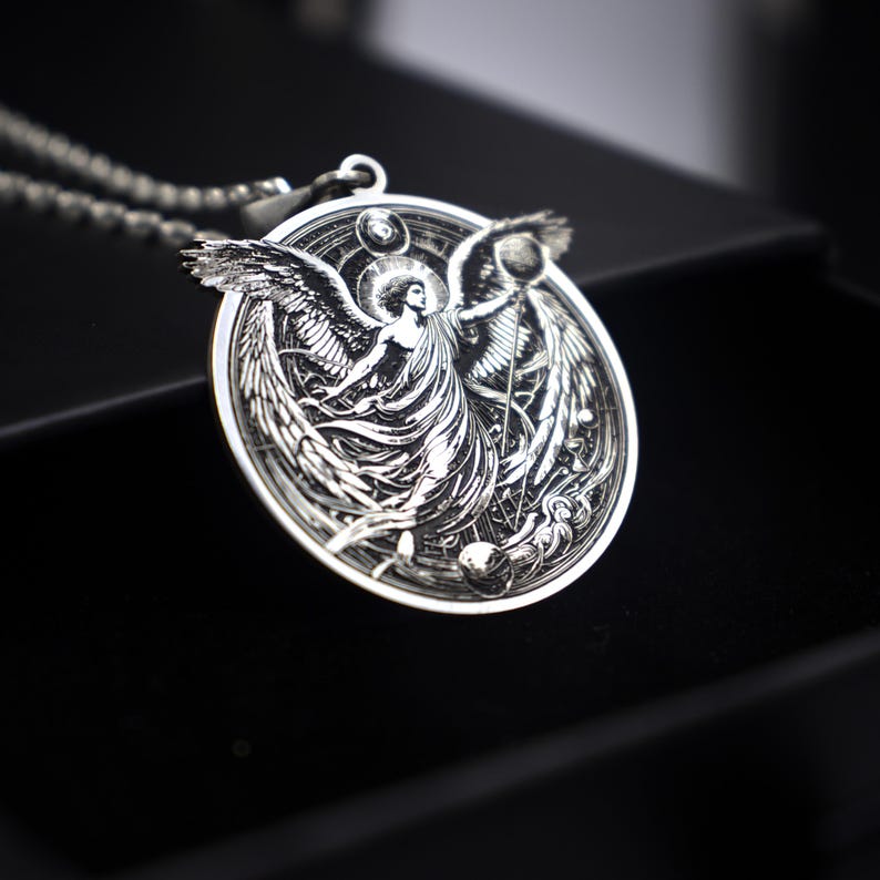 May include: Silver pendant necklace featuring an angel with wings outstretched, holding a sphere. The angel is surrounded by a circular design with celestial bodies.