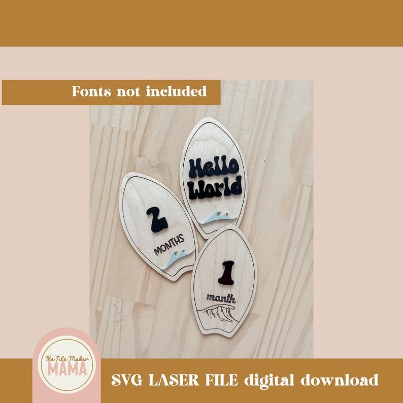 May include: Three wooden surfboard-shaped baby milestone markers. The markers are painted in a light wood colour and feature black text. The text on the markers reads "Hello World", "1 month", and "2 months".