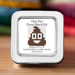 May include: A cross-stitch kit in a silver tin. The kit features a brown and white cross-stitched poop emoji design. The text "Tiny Poo Cross Stitch Kit" is above the design. The kit is approximately 0.9" x 1.0" and contains fabric, needle, thread, and instructions.