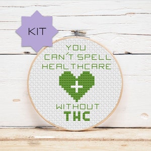 May include: A cross-stitch embroidery hoop kit with a white background and green text that reads "You can't spell healthcare without THC". A green heart with a white cross is in the center of the hoop.