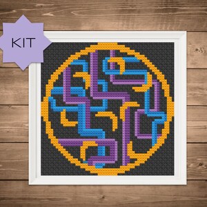 May include: A cross-stitch pattern with a circular design featuring a maze-like pattern in purple, blue, and yellow against a black background. The pattern is framed in a white frame.