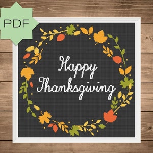 May include: Cross stitch pattern featuring a wreath of autumn leaves and the text "Happy Thanksgiving" on a black background.