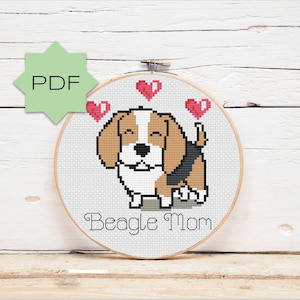 May include: A cross-stitch hoop art featuring a smiling beagle with brown, black, and white markings, and three pink hearts above its head. The text "Beagle Mom" is stitched below the dog. A green PDF icon is in the upper left.