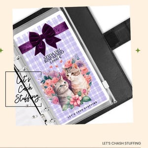 Puede incluir: Una carpeta negra con un inserto decorativo con dos gatos de dibujos animados rodeados de flores. El inserto tiene el texto "SFIDA DEL RISPARMIO 1.000 €" y "Let's Cash Stuffing". Un lazo morado en la parte superior.