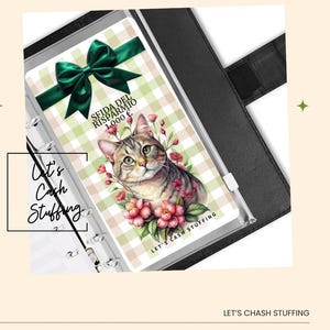 Puede incluir: Un planificador con una ilustración de gato y el texto "SEIDA DEL RISPARMIO 1.000 €". El planificador tiene un lazo verde y las palabras "Let's Cash Stuffing". El planificador está dentro de una carpeta negra.