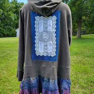 May include: A gray hooded sweatshirt with a denim patch and a white lace design. The sweatshirt has a ruffled hem with a tie-dye pattern in shades of blue and purple.