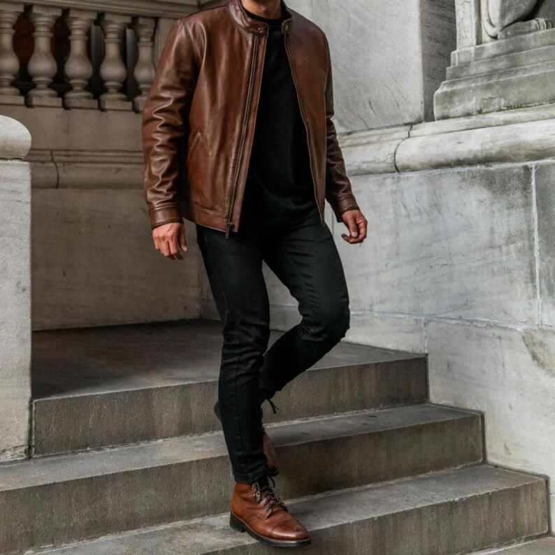 May include: A brown leather jacket with a zipper closure and a black t-shirt underneath. The person is wearing black jeans and brown leather boots.
