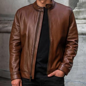 May include: A brown leather jacket with a zipper closure. The jacket has a stand-up collar and long sleeves.