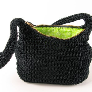 Pu&ograve; includere: Una borsa a mano in crochet nero con chiusura a zip e fodera floreale verde. La borsa ha una tracolla lunga.