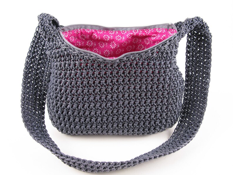 Pu&ograve; includere: Una borsa a tracolla in crochet grigia con chiusura a zip e fodera in tessuto floreale rosa.