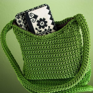 Pu&ograve; includere: Una borsa a tracolla in crochet verde con una pochette in tessuto a motivi bianco e nero all'interno.