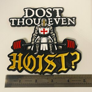 Pu&ograve; includere: Una toppa grafica nera, bianca, rossa e oro raffigurante un cavaliere in armatura che solleva un bilanciere con pesi rossi. Il testo recita DOST THOU EVEN HOIST? Un righello in acciaio inox mostra una larghezza di circa 12,7 cm.