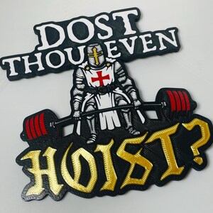 Pu&ograve; includere: Un cartello da parete nero, bianco, rosso e oro raffigurante un cavaliere in armatura che solleva un bilanciere con pesi rossi. Il testo DOST THOU EVEN &egrave; in alto e HOIST? in basso con un carattere audace e stilizzato su sfondo nero.
