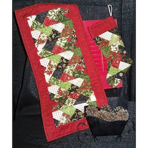 May include: A red quilted table runner with a black, green, and white geometric pattern. The runner is made of fabric scraps and has a festive Christmas theme.