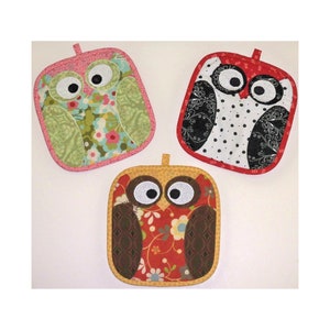 May include: Three quilted oven mitts shaped like owls. The owls are made from different patterned fabrics. One owl is green, pink, and blue. Another owl is black, white, and red. The third owl is brown, red, and yellow.